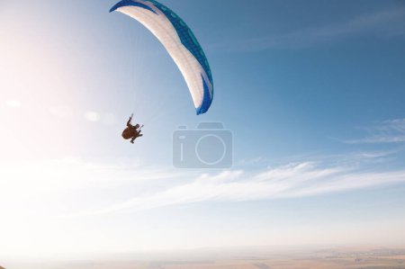 Ein Gleitschirm mit blauem Fallschirm fliegt. Ein männlicher Flieger am Himmel und hebt einen Gleitschirm in die Luft.
