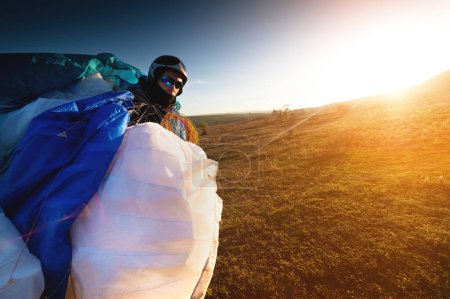 Ein junger Gleitschirmflieger bei Sonnenuntergang in den Bergen sammelt seinen Gleitschirm ein, um ihn zum Ausgangspunkt zu bringen. Gleitschirmsport.