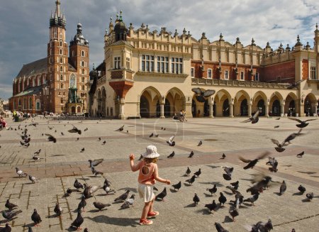 Téléchargez les photos : Cracovie, Pologne - 08 juin 2021 : Cloth Hall ; Sukiennice, place Rynek Glowny dans le centre-ville historique de Cracovie. Enfant et pigeons au premier plan. - en image libre de droit