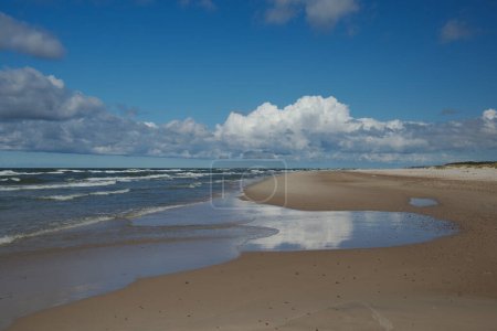 Beautiful seaside landscape, an empty beach, the foamy water of the Baltic Sea, blue sky with white clouds. Slowinski National Park, Poland.