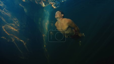 Téléchargez les photos : L'homme plonge dans la rivière d'eau douce avec des rayons ensoleillés qui brillent dans l'eau - en image libre de droit