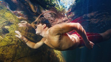 Téléchargez les photos : L'homme plonge dans la rivière d'eau douce avec des rayons ensoleillés qui brillent dans l'eau - en image libre de droit
