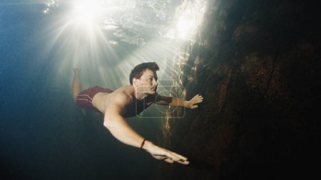Foto de El hombre se sumerge en el río de agua dulce con rayos soleados brillando a través del agua - Imagen libre de derechos