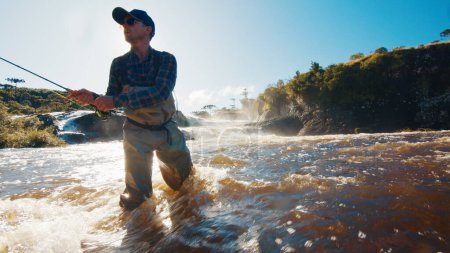 Foto de Pesca con mosca. Pescador en vadeadores lanza la línea en el río turbio rápido - Imagen libre de derechos