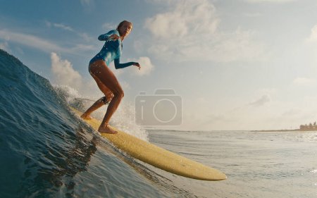 Mujer delgada surfista monta la ola. Mujer surfea la ola oceánica en las Maldivas en longboard amarillo