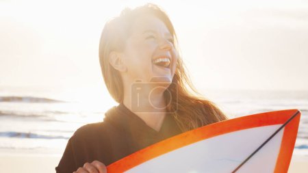 Foto de Mujer surfista se para con tabla de surf en la playa tropical y ríe - Imagen libre de derechos