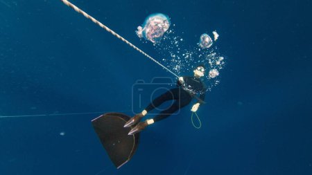 Photo for Freediving on the rope in a sea. Male freediver makes bubbles underwater - Royalty Free Image