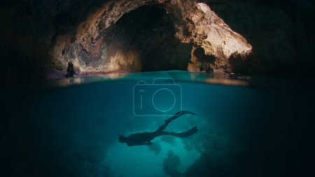 Téléchargez les photos : Le plongeur nage sous l'eau dans la grotte. Male freediver explore la grotte et nage sous l'eau à l'intérieur - en image libre de droit