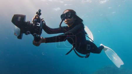 Photo for Female Indian underwater photographer swims with big underwater camera. Female freediver with camera swims in the sea - Royalty Free Image