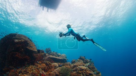 Photo for Underwater photographer takes pictures of the healthy coral reef. Freediver with camera swims over the reef. Nusa Penida, Bali, Indonesia - Royalty Free Image
