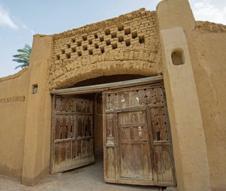 Téléchargez les photos : Ancienne porte d'entrée rustique en bois dans le mur de la maison traditionnelle égyptienne en brique de boue - en image libre de droit