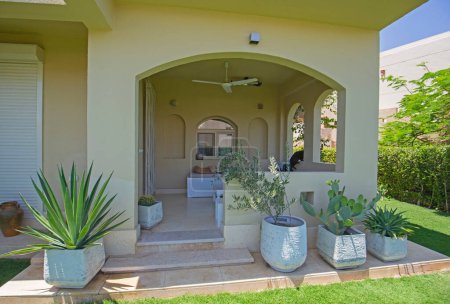 Téléchargez les photos : Extérieur de villa de luxe montrer la maison dans la station balnéaire tropicale d'été montrant patio avec sièges et jardin - en image libre de droit