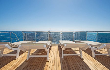 Terrasse arrière en teck d'un grand yacht à moteur de luxe en mer avec chaises longues et fond de vue sur l'océan tropical