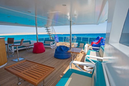 Terrasse arrière en bois de teck d'un grand yacht à moteur de luxe avec chaises canapé table et fond vue sur la mer tropicale