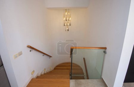 Téléchargez les photos : Vue sur un escalier en bois courbé dans une maison de luxe moderne avec lustre et balustrade en verre - en image libre de droit