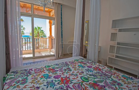 Téléchargez les photos : Décoration d'intérieur ameublement de luxe montrer la maison chambre à coucher montrant des meubles et lit double à baldaquin avec vue sur la mer tropicale - en image libre de droit