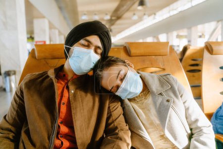 Photo for Indian couple wearing face masks sleeping while sitting in airport indoors - Royalty Free Image