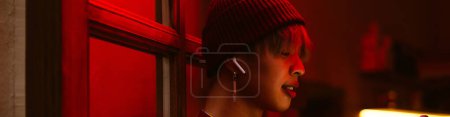 Asian boy listening music with earphones while standing in doorway Poster 619987704