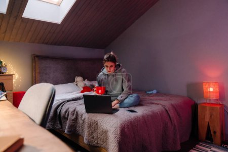 Foto de Chica blanca beber té y el uso de la computadora portátil mientras descansa en la cama en casa - Imagen libre de derechos