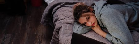 Foto de Mujer joven con pendientes de túnel usando el ordenador portátil mientras está acostado en la cama en casa - Imagen libre de derechos