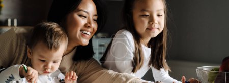 Photo for Young asian woman smiling while spending time with her children at home - Royalty Free Image