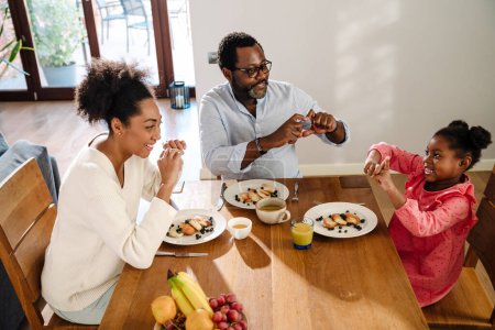 Téléchargez les photos : Femme de famille afro-américaine et homme avec petite fille souriante et petit déjeuner à la maison - en image libre de droit