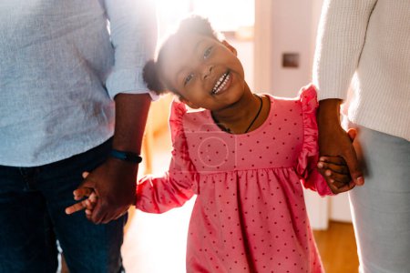 Téléchargez les photos : Femme de famille afro-américaine et homme avec une petite fille souriante et tenant la main à la maison - en image libre de droit
