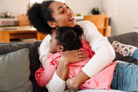 Foto de Africano americano feliz adulto mujer sonriendo y abrazando a su hija chica en casa - Imagen libre de derechos