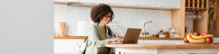 Photo for African american young woman with curly afro hairstyle and eyeglasses using laptop at home - Royalty Free Image
