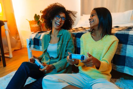 Foto de Feliz mujer afroamericana y su hija adolescente jugando videojuegos con controladores en casa - Imagen libre de derechos