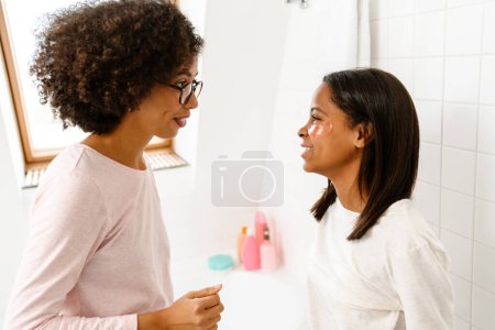 Téléchargez les photos : Heureuse femme afro-américaine et sa fille adolescente faisant des soins de beauté dans la salle de bain - en image libre de droit