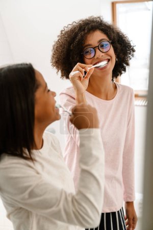 Foto de Negro chica y su madre riendo mientras cepillarse los dientes en cuarto de baño en casa - Imagen libre de derechos