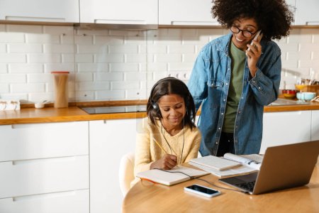 Téléchargez les photos : Jeune femme afro-américaine et sa fille adolescente faisant leurs devoirs ensemble à la maison - en image libre de droit