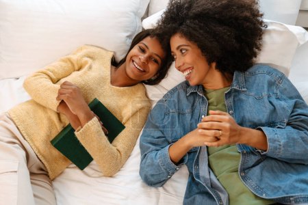 Foto de Negro chica y su madre riendo y hablando mientras acostado en cama en casa - Imagen libre de derechos