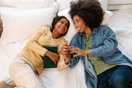 Foto de Negro chica y su madre riendo y hablando mientras acostado en cama en casa - Imagen libre de derechos