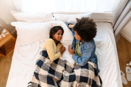 Foto de Negro chica y su madre hablando juntos mientras acostado en cama en casa - Imagen libre de derechos