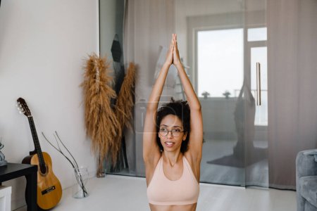 Téléchargez les photos : Femme noire portant des lunettes faisant de l'exercice pendant la pratique du yoga à la maison - en image libre de droit