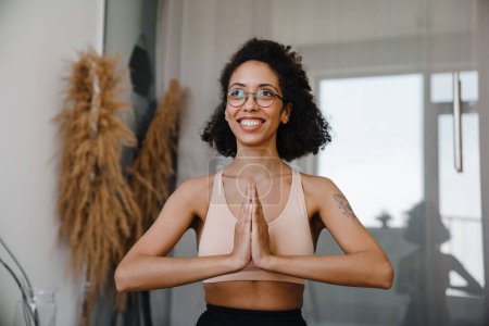 Photo for Black woman wearing eyeglasses doing exercise during yoga practice at home - Royalty Free Image