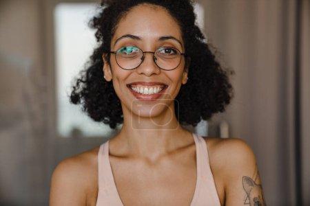 Foto de Mujer joven negra con anteojos sonriendo mientras hace ejercicio en casa - Imagen libre de derechos
