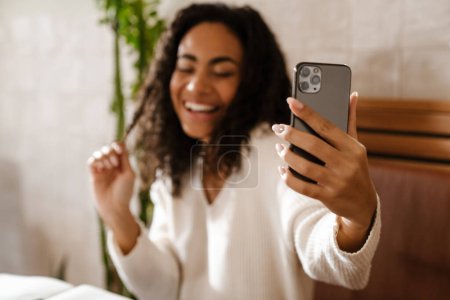 Photo for Young black woman laughing and taking selfie photo on cellphone in cafe indoors - Royalty Free Image