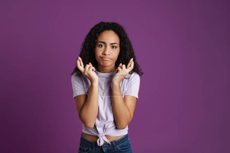 Téléchargez les photos : Jeune femme noire tenant les doigts croisés pour la bonne chance isolé sur fond violet - en image libre de droit