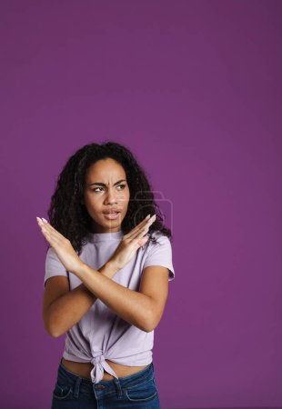 Foto de Joven mujer negra frunciendo el ceño mientras muestra un gesto de stop aislado sobre fondo púrpura - Imagen libre de derechos