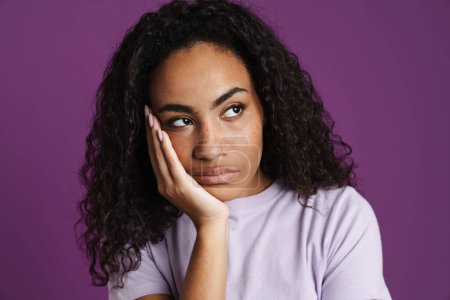 Photo for Young black woman propping up her head and looking aside isolated over purple background - Royalty Free Image