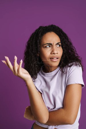 Photo for Perplexed black woman gesturing and looking aside isolated over purple background - Royalty Free Image