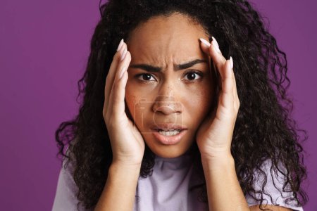 Téléchargez les photos : Jeune femme noire aux cheveux ondulés exprimant surprise à la caméra isolée sur fond violet - en image libre de droit