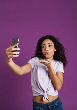 Photo for Young black woman gesturing while taking selfie on mobile phone isolated over purple background - Royalty Free Image