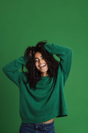 Téléchargez les photos : Jeune femme noire riant tout en tenant sa tête isolée sur fond vert - en image libre de droit