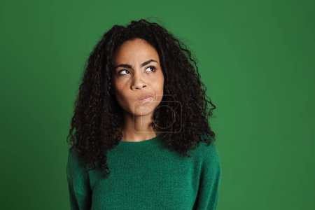 Photo for Young black woman with wavy hair frowning and looking aside isolated over green background - Royalty Free Image