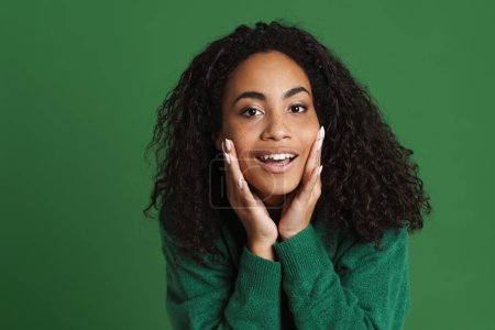 Foto de Joven mujer negra con sonrisa y tocando su piel aislada sobre fondo verde - Imagen libre de derechos