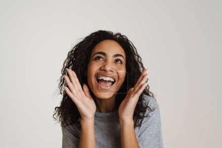 Téléchargez les photos : Jeune femme noire aux cheveux ondulés riant et gesticulant isolé sur fond blanc - en image libre de droit